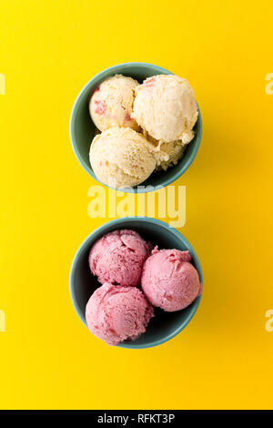 Tasty ice cream vanilla strawberry scoops in blue bowls on yellow vibrant background. Top View. Stock Photo