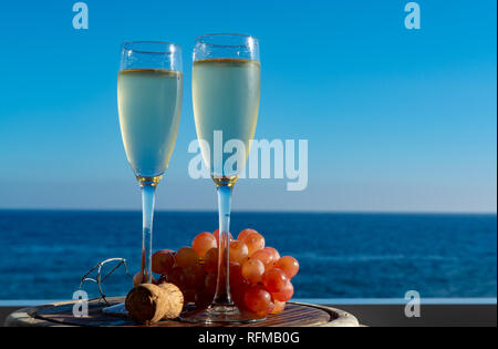 Champagne, prosecco or cava served with pink grape in two glasses on outside terrace with sea view close up Stock Photo