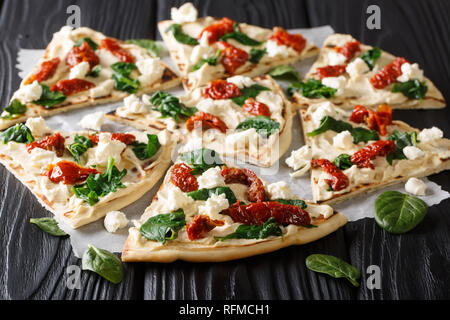 Flat bread with hummus, sun-dried tomatoes, spinach and goat cheese close-up on the table. horizontal Stock Photo