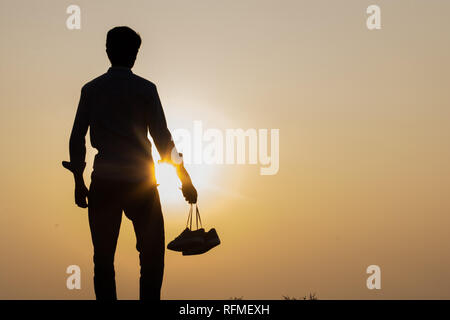 The Boy standing at sunset and holding shoes in his hand Close-up Stock Photo