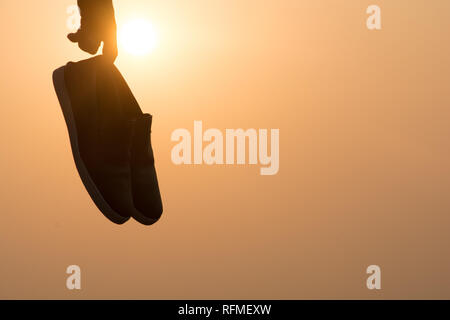 The Boy standing at sunset and holding shoes in his hand Close-up Stock Photo