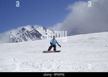 Snowboarder downhill on ski slope in high snowy mountains at sun winter day. Caucasus Mountains in fog, region Dombay. Stock Photo