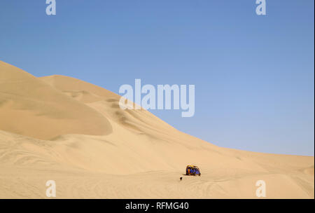 Running dune buggy chasing by a naughty dog on the sand dunes of Huacachina desert, Ica region, Peru Stock Photo