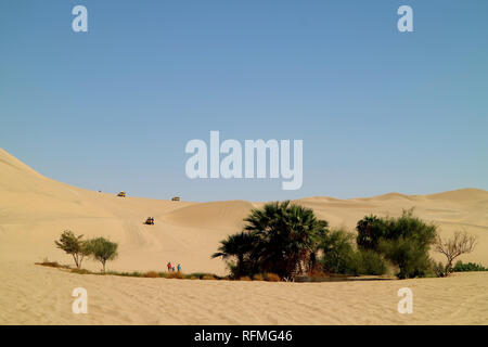 People enjoy the activities around the small oasis on the immense sand dunes of Huacachina desert, Ica region, Peru Stock Photo