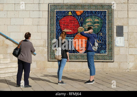 Tourist looking at a mosaic model by Armenian ceramicist Arman Darian depicting the Bunting Clover Leaf Map, also known as The World in a Cloverleaf, an historic mappa mundi drawn by the German Protestant pastor, Heinrich Bünting. in which Jerusalem is in the centre of the map surrounded by the three continents, comprising three leaves of a clover shape installed on the fence of Safra Square at the site of Jerusalem's city hall. Israel Stock Photo