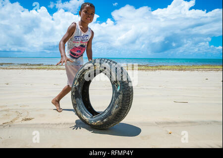 BAHIA, BRAZIL - FEBRUARY 15, 2017: A young Brazilian rolls a tire as a game along a an empty beach on a remote island in rural Nordeste. Stock Photo