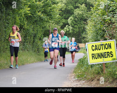 Female runners taking part in a ladies road running race with a 'caution runners' sign on the road Stock Photo