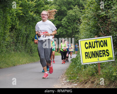 Female runners taking part in a ladies road running race with a 'caution runners' sign on the road Stock Photo