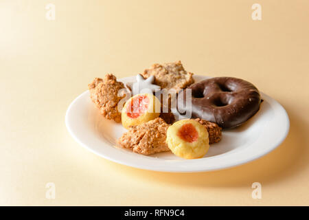 star-shaped cinnamon biscuits, gingerbread and macaroons on a white plate, isolated on beige Stock Photo