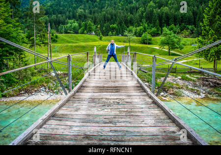 happy distant woman jump of a wooden pedestrian bridge footbridge over river Soca in Slovenia in  wild nature background