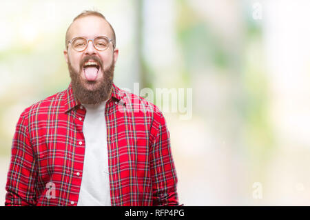 Young caucasian hipster man wearing glasses over isolated background sticking tongue out happy with funny expression. Emotion concept. Stock Photo