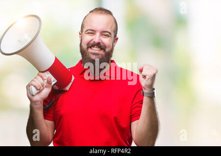 Young caucasian man shouting through megaphone over isolated background screaming proud and celebrating victory and success very excited, cheering emo Stock Photo