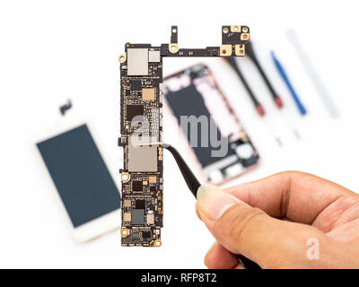 Close-up of technician hand clamping smartphone logic board on blurred smartphone component background Stock Photo