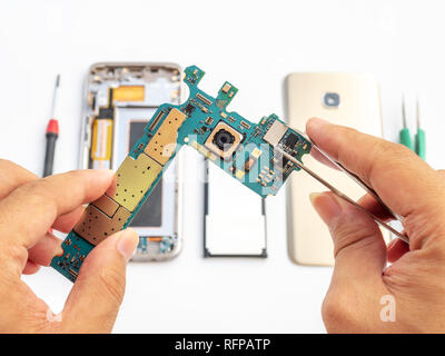 Close-up of technician holdinging smartphone logic board and clamping micro processor on blurred smartphone component background Stock Photo