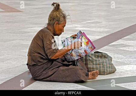 Old woman reading a cartoon, Shwedagon Pagoda, Yangoon, Rangun, Myanmar, Burma Stock Photo