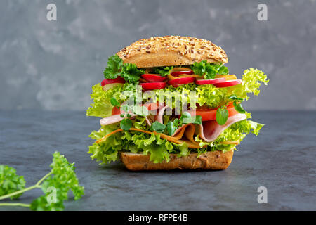 Big sandwich with ham, cheese and fresh vegetables on a dark board. Breakfast concept. Stock Photo