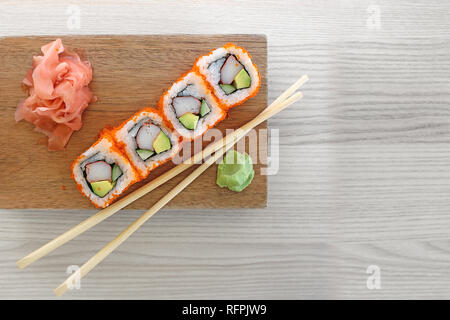 Maki sushi rolls with chopsticks on a wooden plate with wasabi and pickled ginger. Top view of restaurant sushi, isolated on grey wood backdrop. Stock Photo