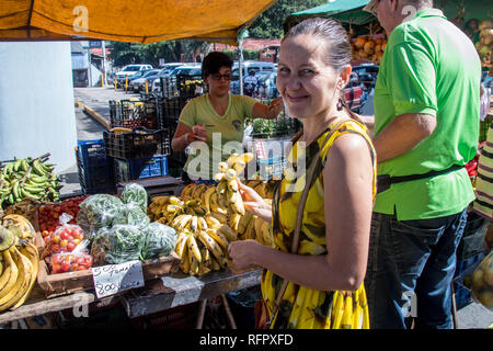 A portrait of a beautiful woman in a yellow dress buying bananas at the sunday's farmers market in Santa Ana, Costa Rica. Stock Photo