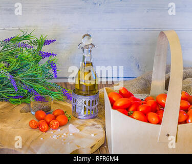 Cherry tomatoes in a cardboard  basket   with thyme,  olive oil , Himallayan pink salt on a wooden surface . Lavender flowers in the background. stock Stock Photo
