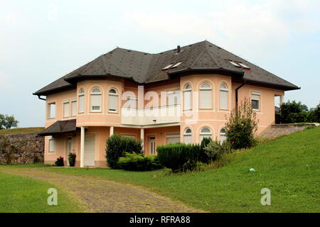 New suburban family house shaped like small light pink castle with closed white blinds on windows and new roof tiles surrounded with cut grass Stock Photo