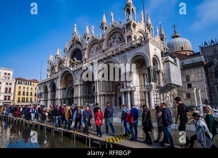 Many tourists are walking on footbridges in front of Saint Mark's Basilica, Basilica di San Marco, San Marco Square, Piazza San Marco flooded during t Stock Photo