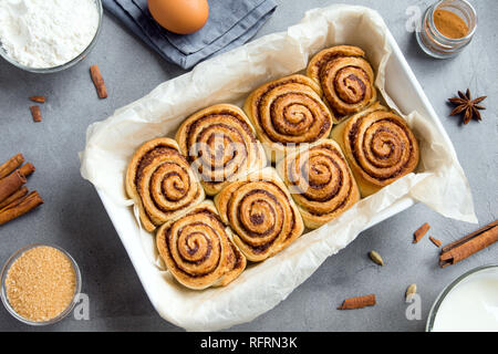 Cinnamon rolls or cinnabon, homemade recipe of sweet traditional dessert buns with pastry ingredients on grey stone background. Stock Photo