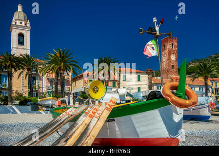 Old colorful wooden fishing boats on the beach, Noli, Italy with historic medieval waterfront buildings behind and tropical palm trees on the promenad Stock Photo