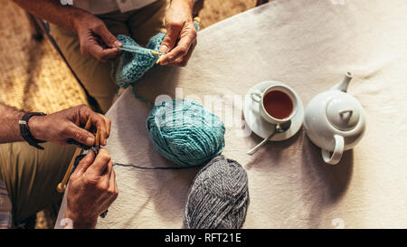 Top view of senior men hands knitting with teapot and teacup on table. Close up of retired men hands with knitting needles and wool yarns. Stock Photo