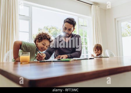 Man sitting at the table at home with his kids taking care of them. Father helping his son in his studies. Stock Photo