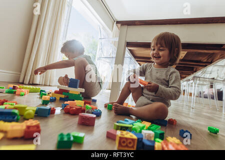 Happy kids playing with building blocks sitting on floor. Two kids playing with toys at home. Stock Photo