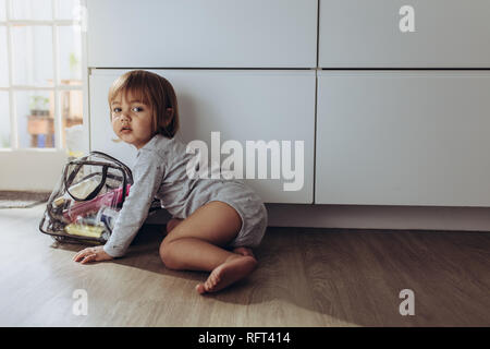 Kid crawling on floor playing with a bag containing cosmetics. Little kid sitting on floor playing alone. Stock Photo