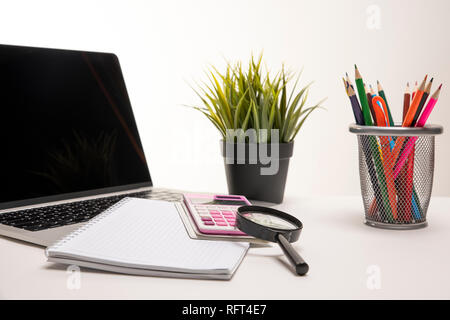 Desk having a laptop, calculator, organizer, crayons, magnifier, notepad and a green plant. Modern business office for commercial Stock Photo