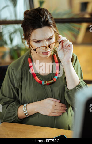 Pregnant woman putting glasses on while working in office Stock Photo