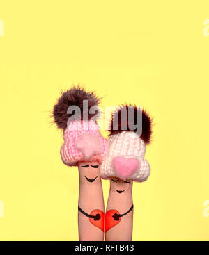 Family concept - a man and a woman hold on the red heart, painted at fingers and isolated on yellow background. Valentine Day. Stock Photo