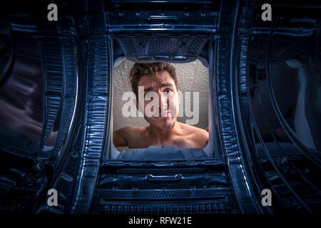 Young man doing laundry View from the inside of broken washing machine Stock Photo