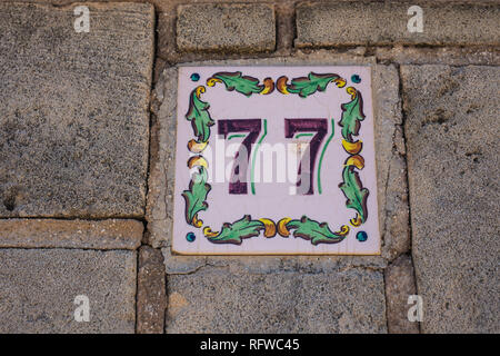 House number seventy-seven 77 painted on ceramic tile in blue and black with fleur-de-lis pattern from Sweden or Belgium Stock Photo