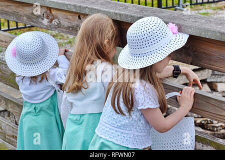 Three young caucasian girls in matching outfits and hats looking over wooden fence at pier Stock Photo