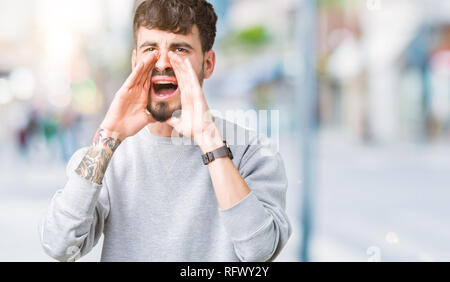 Young handsome man wearing sweatshirt over isolated background Shouting angry out loud with hands over mouth Stock Photo