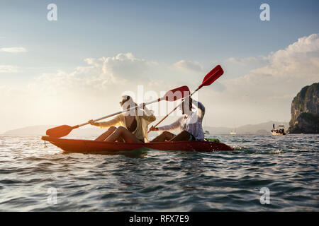Happy couple walks by sea kayak or canoe at sunset bay. Kayaking or canoeing concept with people Stock Photo
