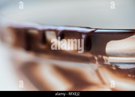 Macro closeup of liquid creamy smooth dark brown chocolate syrup icing in glass mixing bowl isolated dripping off sides edge Stock Photo