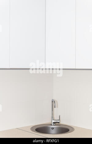 New modern faucet and kitchen room sink closeup with round stainless steel basin and countertop in model house home apartment and white vertical count Stock Photo