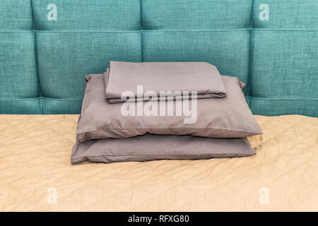 Hotel bed with green blue headboard and pillows in bedroom in home house or apartment with sheets stack closeup Stock Photo