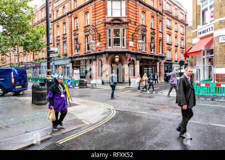 London, UK - September 12, 2018: Woman and business people man walking in rainy city weather on sidewalk by Brewer street wet road shopping in SoHo du Stock Photo