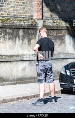 London, UK - September 13, 2018: Street in Belgravia area with candid man security guard standing with phone on pavement by car Stock Photo