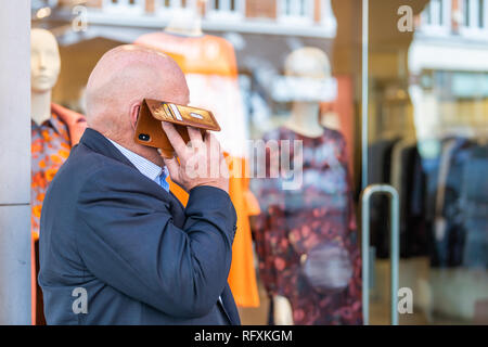 London, UK - September 13, 2018: Business man talking on phone in Chelsea with background of retail fashion store shop Stock Photo