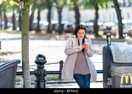 London, UK - September 13, 2018: Chelsea park area with people on street pavement pedestrians and woman standing smoking break looking at phone Stock Photo