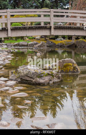 iew of mossy rocks and koi pond with arched bridge at Kasugai Gardens, a Japanese garden in downtown Kelowna, British Columbia, Canada Stock Photo