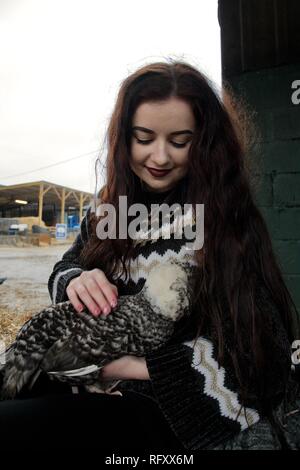 Long haired girl on a farm cuddles a fluffy chicken Stock Photo