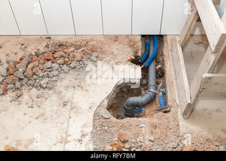 Repair plastic polypropylene gray sewer pipes in the hole in the brick floor with broken tiles. Concept of pipe replacement, water leakage, transfer o Stock Photo