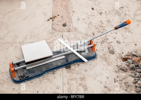 Closeup professional metal construction tile cutter and lying on the floor on a dusty construction site. Concept decoration and repair of bathroom, ki Stock Photo